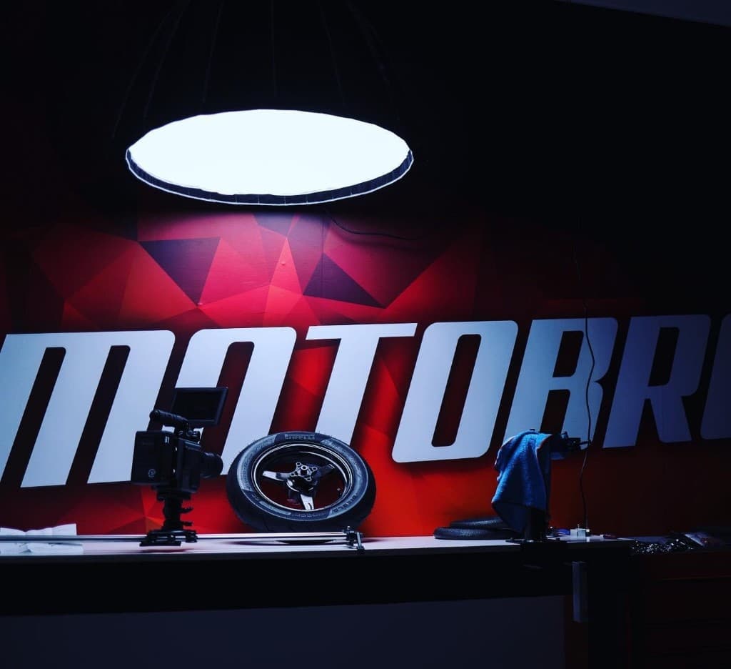 MotoBros shop wall with branded signage, motorcycle wheel, and professional camera setup